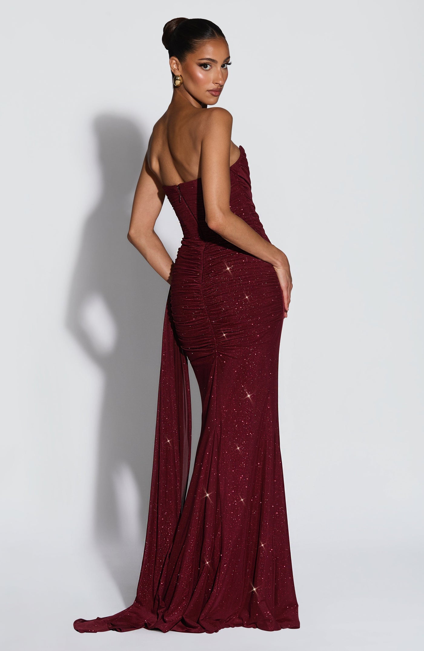 Woman wearing a burgundy evening gown with a slit on a white background